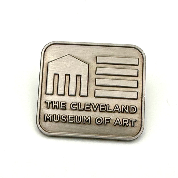 A square-shaped antique nickel lapel pin with the engraved text 'THE CLEVELAND MUSEUM OF ART'.