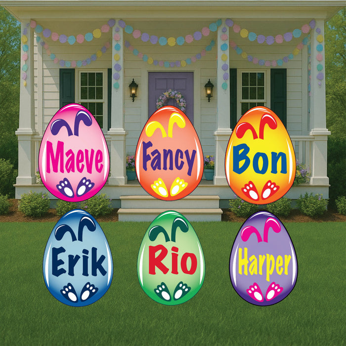 A series of colorful wooden Easter eggs displayed in a garden, each with a different name personalized on them, leading up to a front porch with Easter decorations.